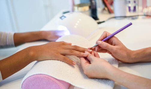 Close-up of beautician painting a woman's nails with a brush in a nail salon. Costumer receiving a manicure.